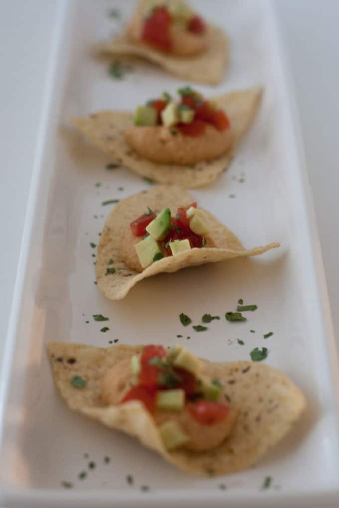 Tortilla chips served on white platter topped with chipotle hummus, tomatoes and avocado