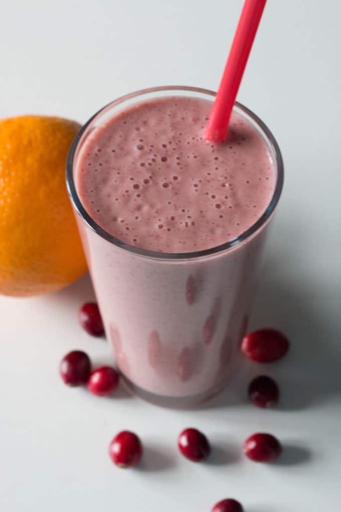 Smoothie in glass surrounded by an orange and fresh cranberries
