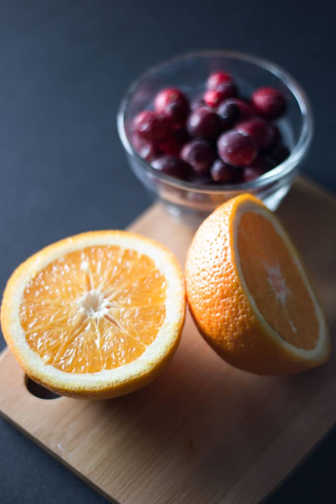 orange cut in half alongside bowl of cranberries