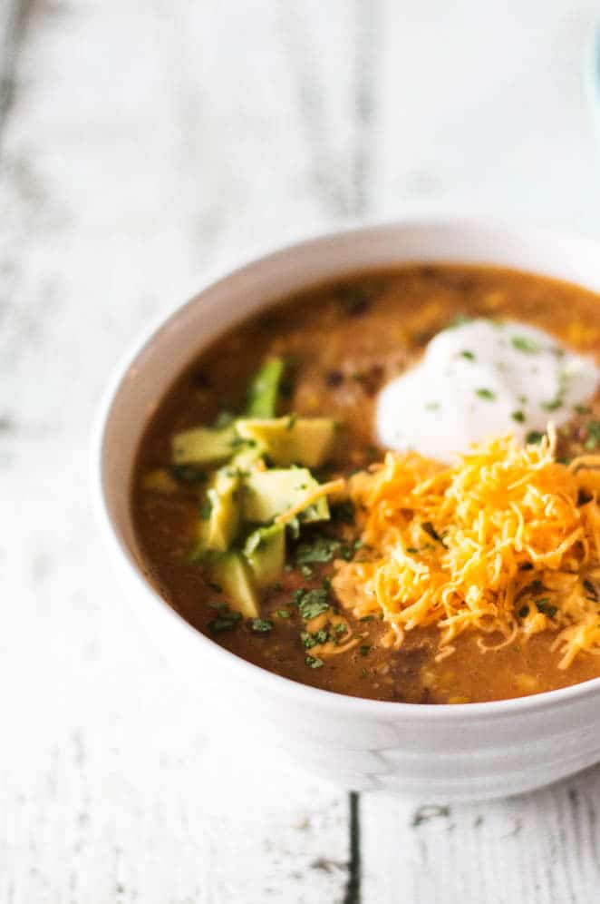 Soup topped with avocado and cheese in white bowl