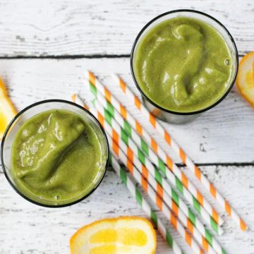 top down view of two glasses of green smoothie surrounded by straws and orange peels