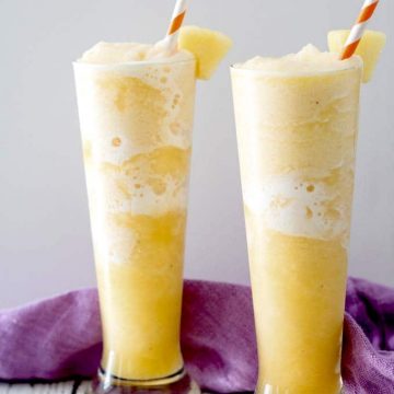 two tall glasses filled with yellow coloured slush with striped straws.