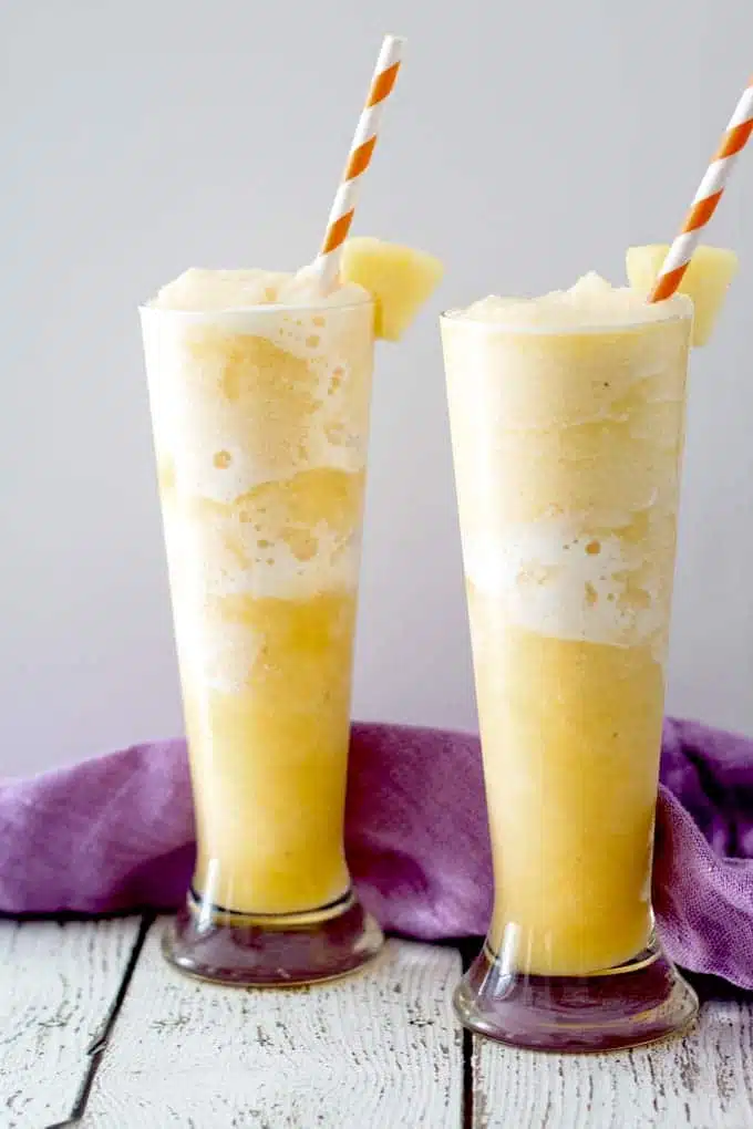 two tall glasses filled with yellow coloured slush with striped straws.