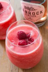 Icy drink topped with raspberries with wine bottle in the background.
