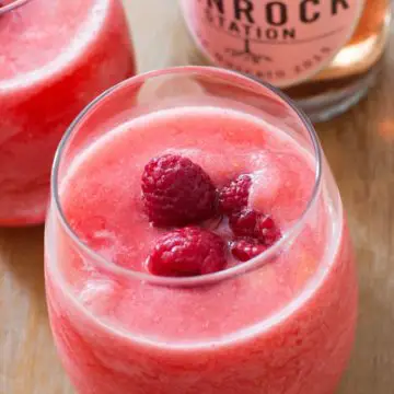 Icy drink topped with raspberries with wine bottle in the background.