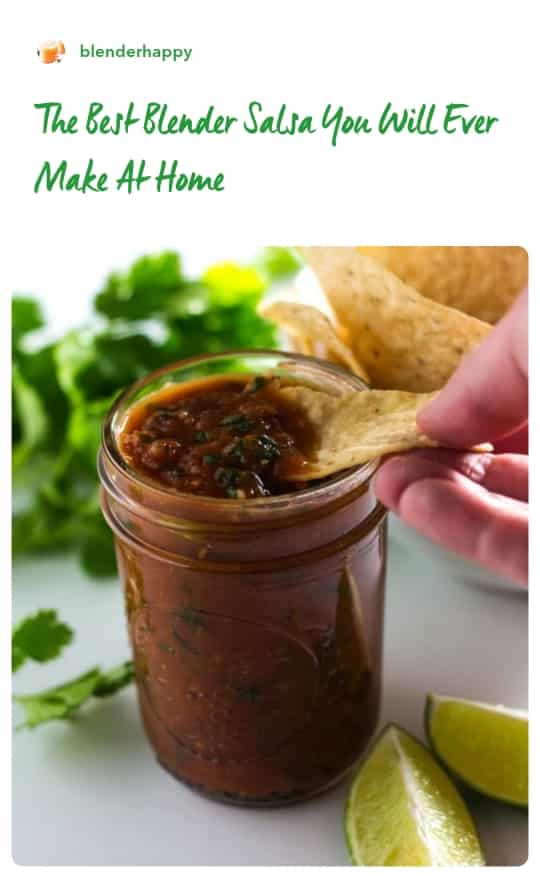 Hand dipping a tortilla chip in a jar of salsa surrounded by fresh cilantro, lime slices and a bowl of tortilla chips