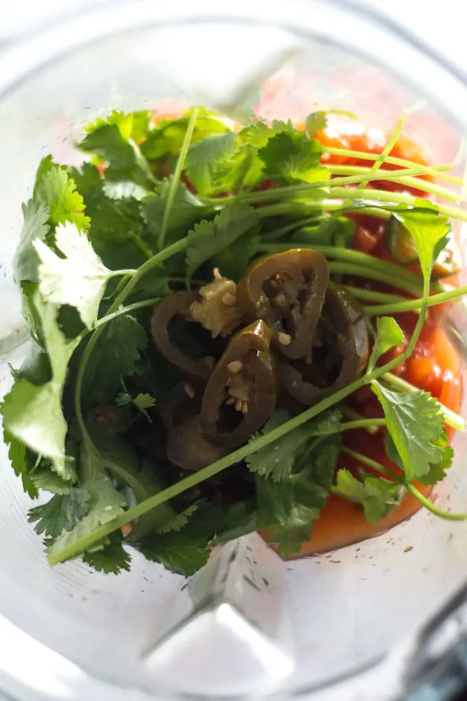 Green cilantro and jalapenos in a blender jar with tomatoes