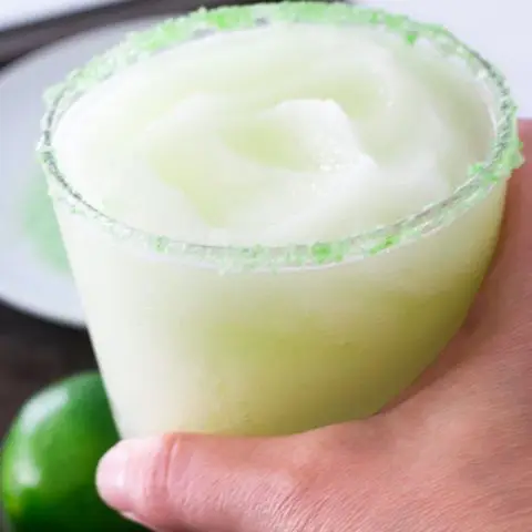 hand holding glass filled with lime margaritas