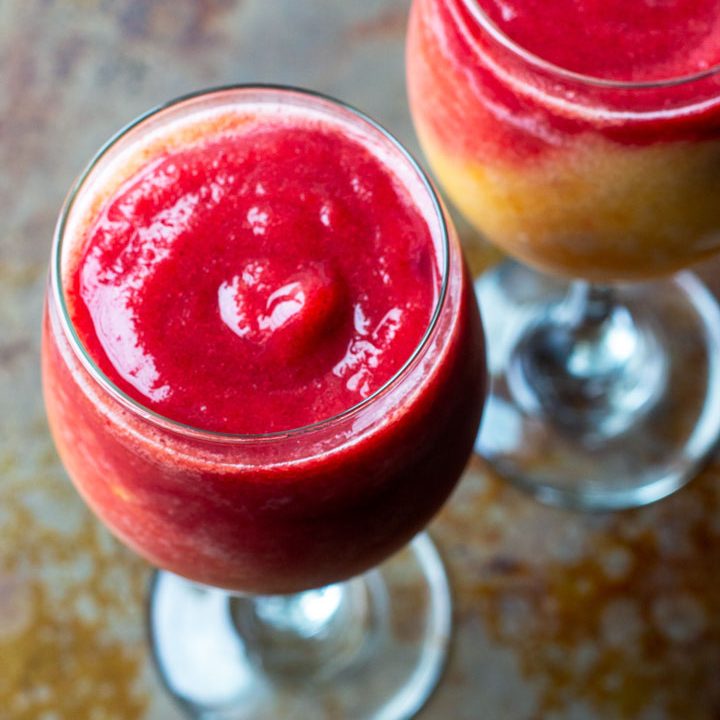 Two wine glasses filled with pink and yellow frozen beverage