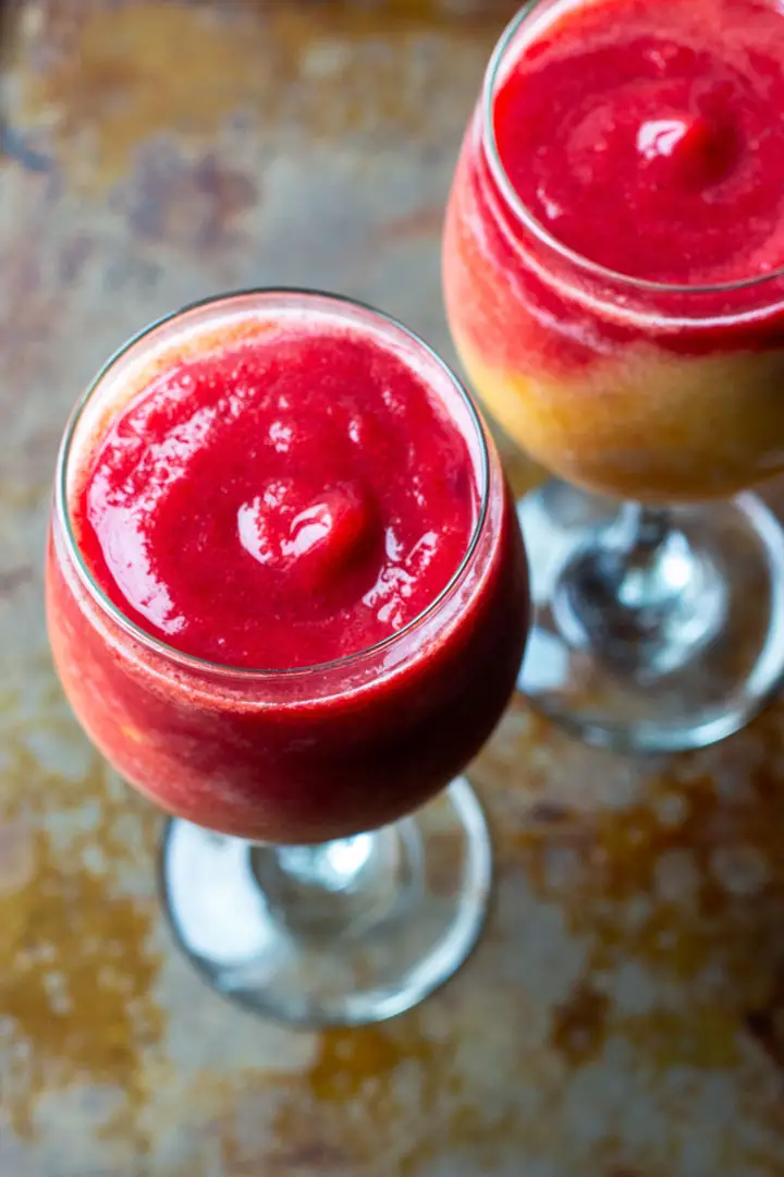 Two wine glasses filled with pink and yellow frozen beverage