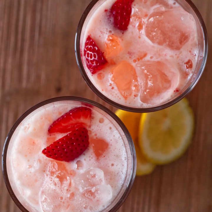 Two glasses filled with lemonade and served with strawberry slices and lemons