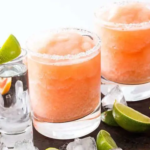 Two frozen paloma drinks surrounded by ice cubes and lime slices