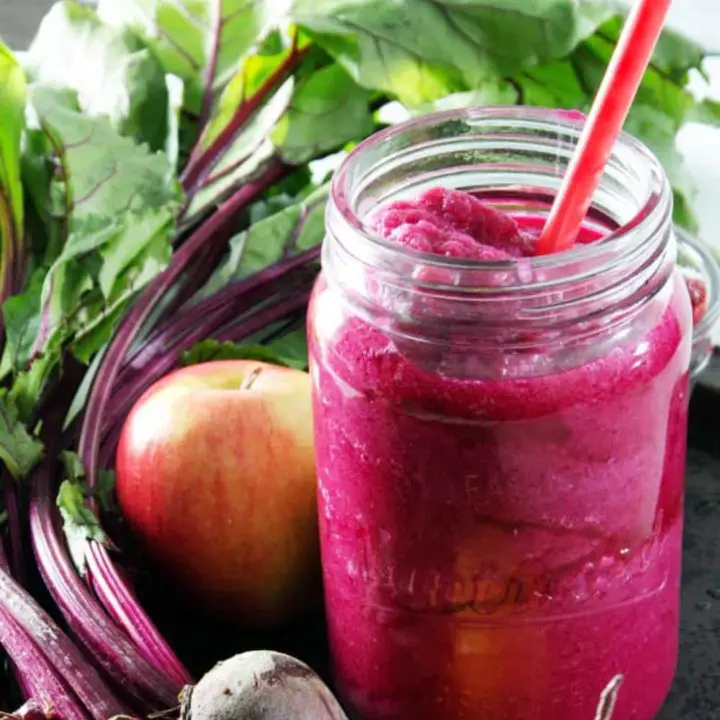 pink smoothie in glass jar surrounded by apple and beets