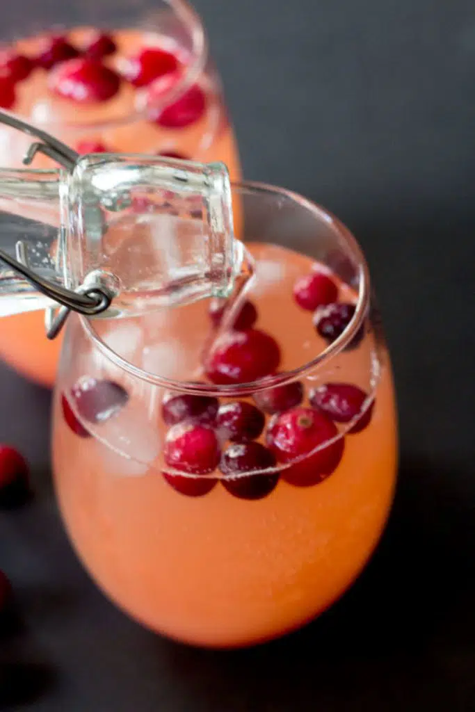 sparkling water being poured into glass with cranberries and ice