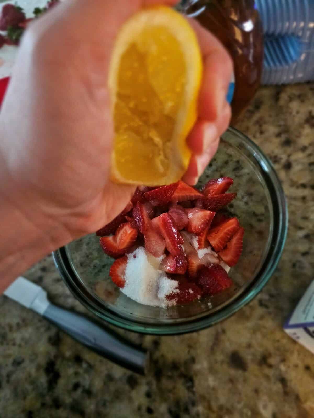 lemon squeezed into bowl with strawberries and sugar